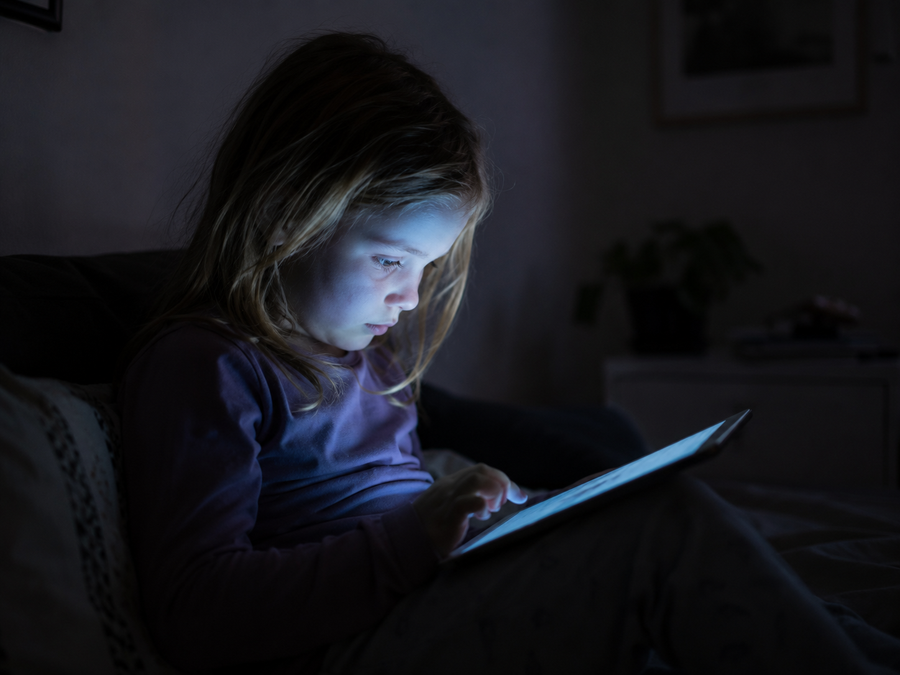 Barn opslugt af tablet-skærm i mørkt rum